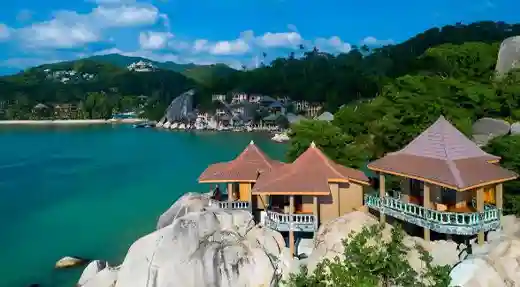 Cliffside bungalows built on granite rocks above a calm turquoise bay on Koh Tao Thailand.