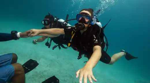 Beginner diver holding an instructor’s hand during SSI Basic Diver underwater training with Echo Divers Koh Tao.