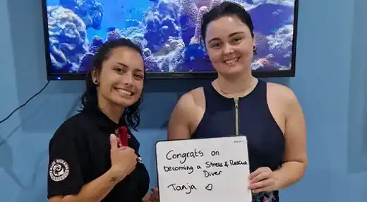 Rescue course student celebrating certification with an instructor at Echo Divers Koh Tao while holding a congratulatory sign.