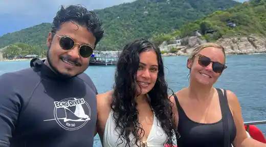 Three smiling divers on the Echo Divers Koh Tao boat, enjoying their day of diving with the island in the background.
