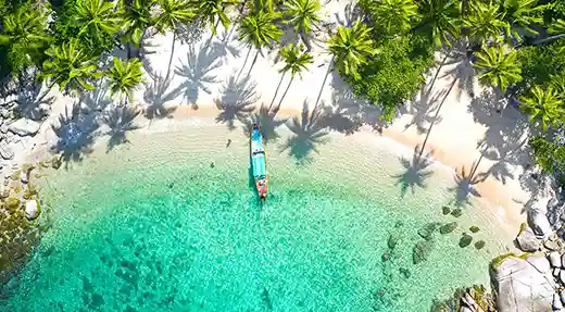 Aerial view of Sai Nuan Beach on Koh Tao Thailand with a longtail boat in clear turquoise water and palm trees along the sand.