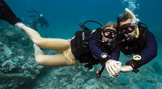  Two Echo Divers Koh Tao students holding hands while diving over a coral reef, captured by Liquid Light Studio during an underwater photo session. 
