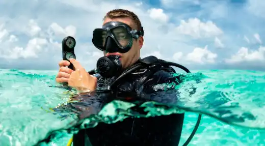 Scuba diver holding a compass at the surface in clear blue water