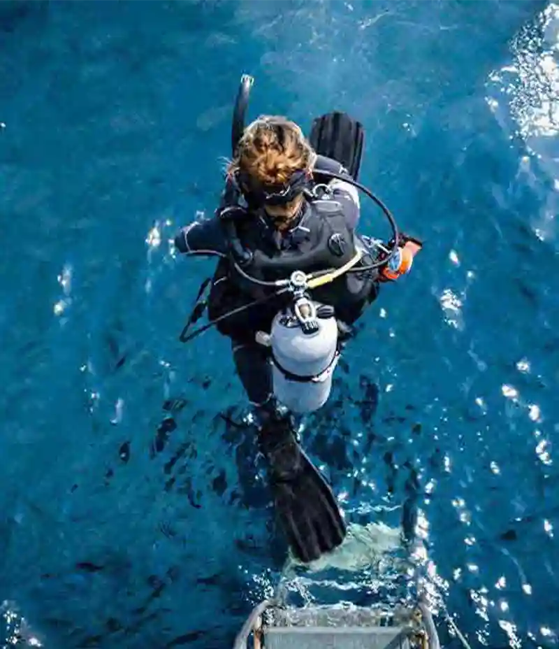 Scuba diver stepping into the sea from a boat ladder ready to descend, Koh Tao, Thailand