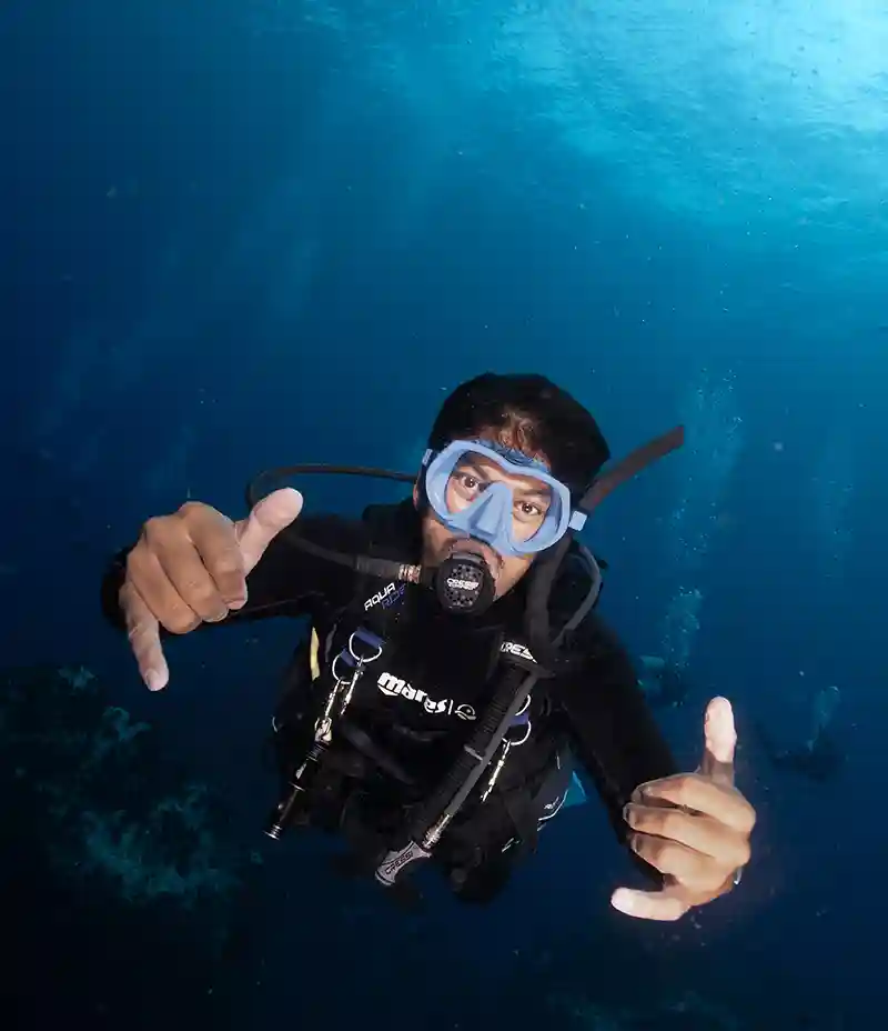 Scuba diver giving a shaka hand sign underwater in blue water above the reef, Koh Tao, Thailand
