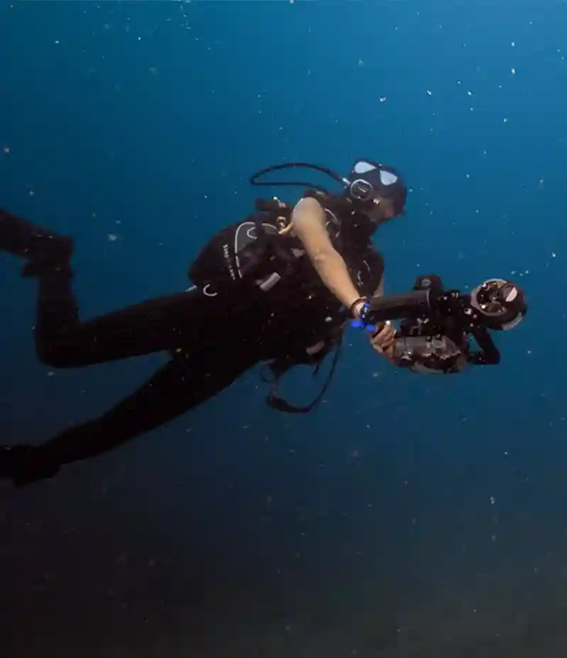 Diver filming underwater with a video camera rig and lights in open blue water, Koh Tao, Thailand